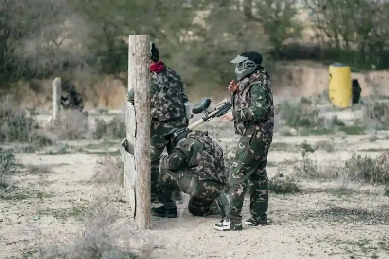 Skupina lidí v maskáčích hrající paintball nebo airsoft v lese